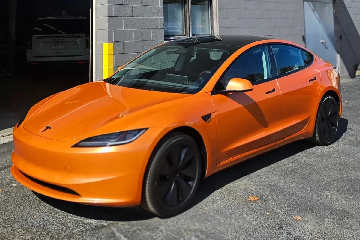 A side view of the same orange Tesla Model 3, showcasing its sleek design and tinted windows.