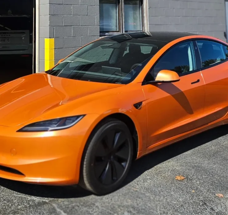 A side view of the same orange Tesla Model 3, showcasing its sleek design and tinted windows.